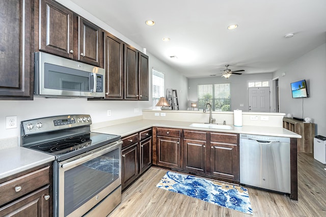 kitchen with stainless steel appliances, light countertops, light wood-style floors, a sink, and a peninsula