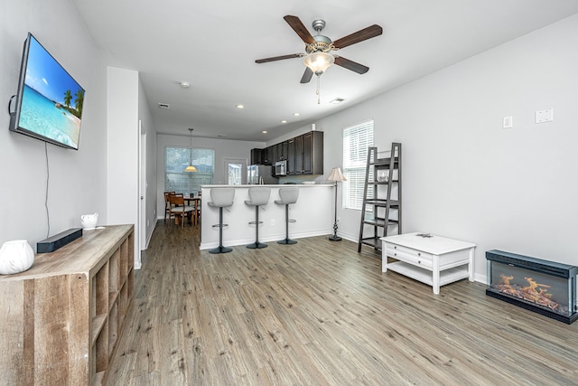 kitchen with ceiling fan, baseboards, appliances with stainless steel finishes, light wood-type flooring, and a kitchen bar