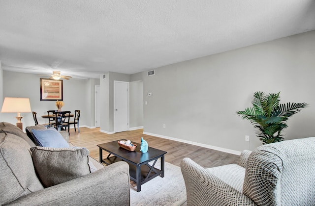 living room featuring a textured ceiling, wood-type flooring, and ceiling fan