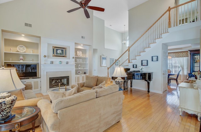 living area featuring a towering ceiling, stairway, ceiling fan, built in shelves, and hardwood / wood-style floors