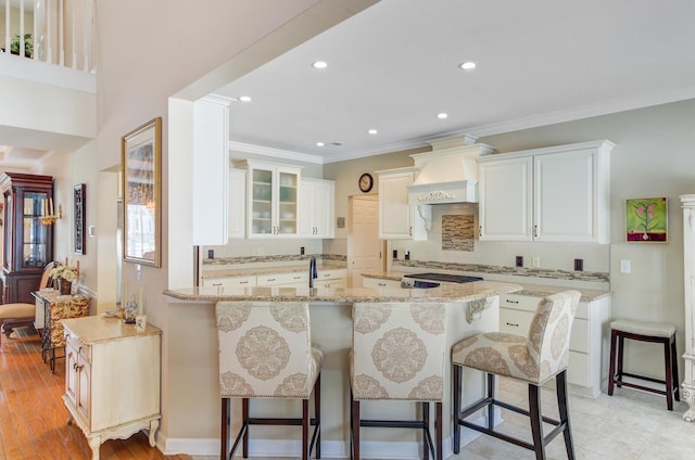 kitchen with premium range hood, a kitchen breakfast bar, tasteful backsplash, light stone counters, and ornamental molding
