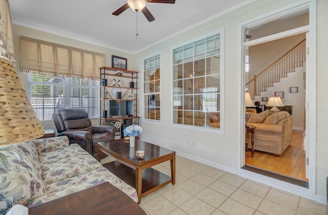living area with ceiling fan, crown molding, stairs, baseboards, and light tile patterned floors