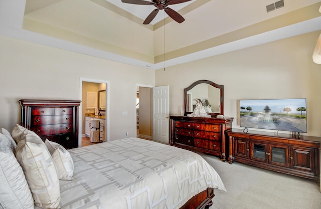 carpeted bedroom featuring a tray ceiling, ensuite bath, and a ceiling fan