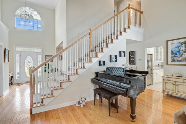 foyer entrance featuring a towering ceiling, stairway, light wood-style flooring, and baseboards