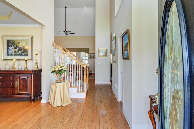 foyer entrance featuring hardwood / wood-style flooring, baseboards, stairs, a towering ceiling, and a ceiling fan