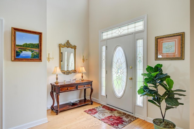 foyer with wood finished floors, a towering ceiling, and baseboards