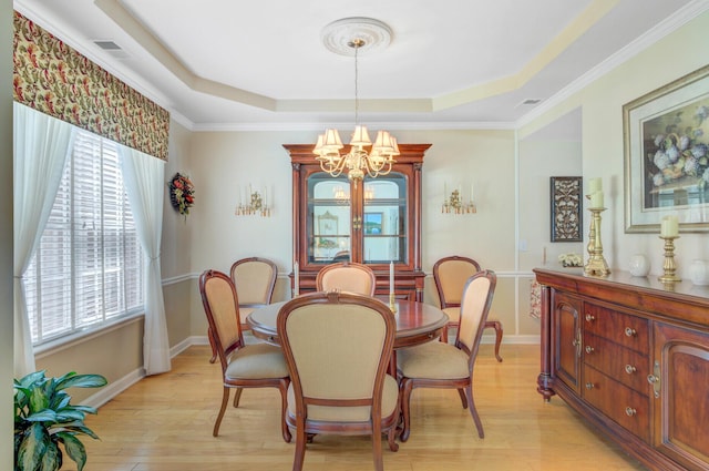 dining area featuring a raised ceiling, light wood-style flooring, a chandelier, baseboards, and ornamental molding