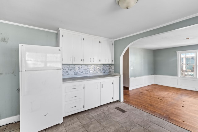 kitchen featuring arched walkways, a wainscoted wall, freestanding refrigerator, light countertops, and white cabinetry