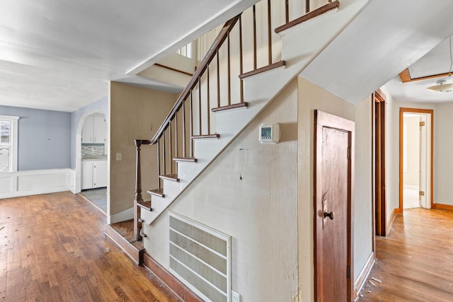 staircase with hardwood / wood-style flooring, baseboards, and arched walkways