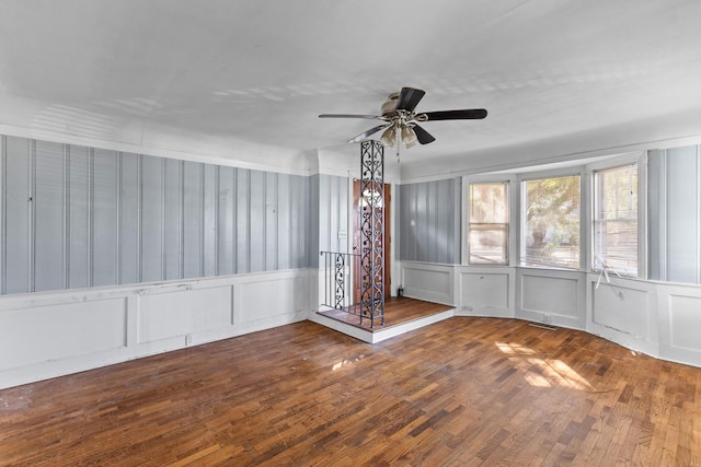 empty room with wood-type flooring, visible vents, a decorative wall, and a ceiling fan