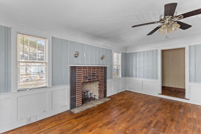 unfurnished living room featuring ceiling fan, a fireplace, a decorative wall, and wood finished floors