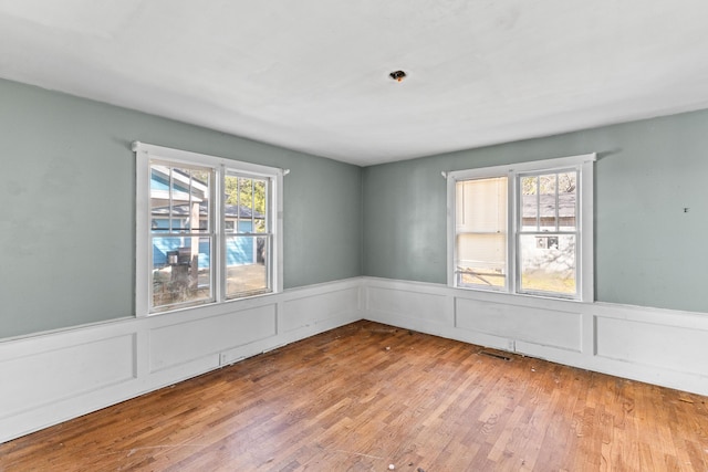 unfurnished room featuring a wealth of natural light, wainscoting, visible vents, and wood finished floors