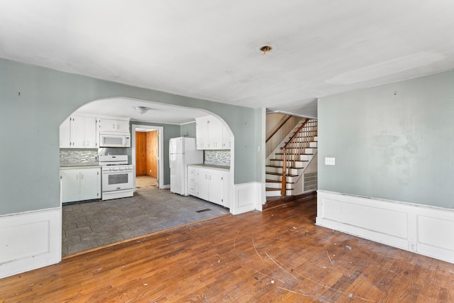 kitchen with dark wood-style floors, backsplash, wainscoting, white cabinetry, and white appliances