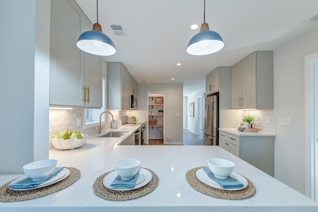 kitchen featuring gray cabinetry, stainless steel fridge, sink, and hanging light fixtures