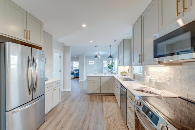 kitchen featuring sink, kitchen peninsula, pendant lighting, decorative backsplash, and appliances with stainless steel finishes