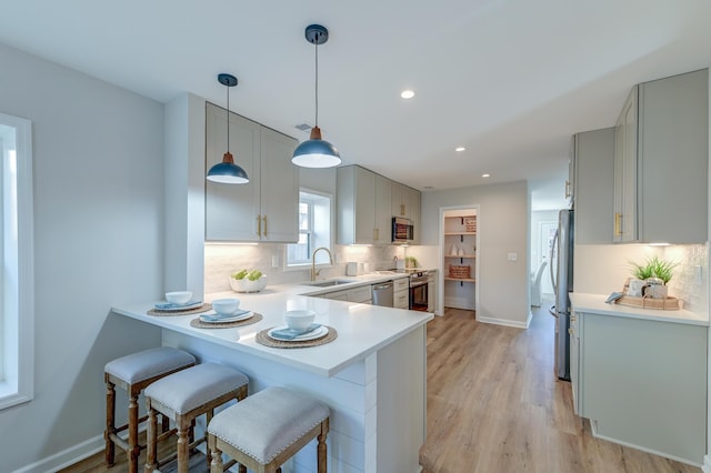 kitchen with kitchen peninsula, appliances with stainless steel finishes, gray cabinetry, sink, and light hardwood / wood-style flooring