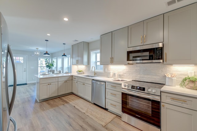 kitchen featuring sink, hanging light fixtures, light hardwood / wood-style floors, kitchen peninsula, and stainless steel appliances