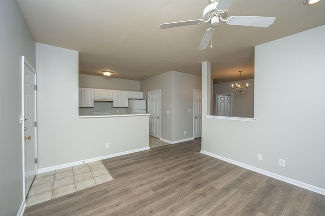 unfurnished living room featuring ceiling fan with notable chandelier and light hardwood / wood-style floors