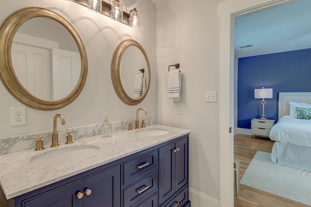 ensuite bathroom featuring a sink, baseboards, double vanity, and wood finished floors