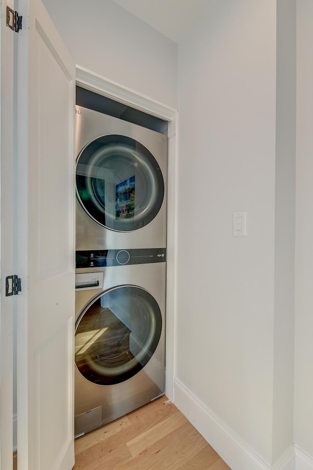laundry room featuring baseboards, laundry area, stacked washing maching and dryer, and wood finished floors