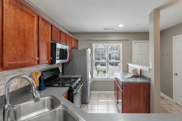 kitchen with light tile patterned floors, a sink, baseboards, appliances with stainless steel finishes, and backsplash