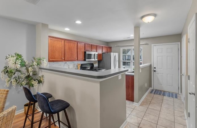 kitchen with a peninsula, baseboards, a kitchen breakfast bar, appliances with stainless steel finishes, and decorative backsplash