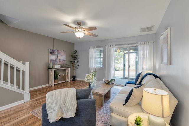 living area featuring visible vents, a ceiling fan, wood finished floors, baseboards, and stairs