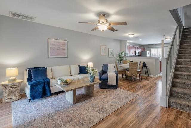 living room with visible vents, stairway, a ceiling fan, wood finished floors, and baseboards