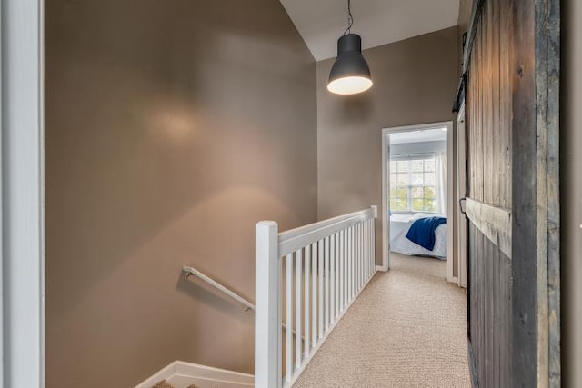 hallway with a barn door, carpet flooring, vaulted ceiling, an upstairs landing, and baseboards