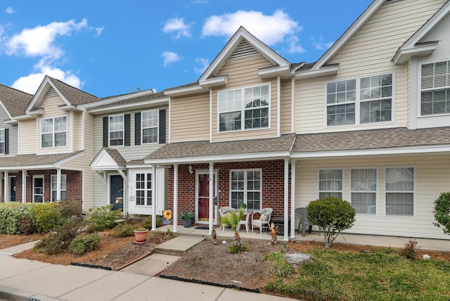 townhome / multi-family property featuring roof with shingles, a porch, and brick siding