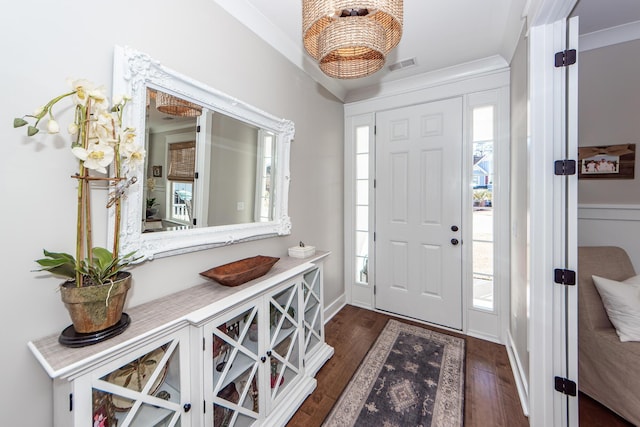 foyer entrance with dark wood-type flooring, a wealth of natural light, and ornamental molding