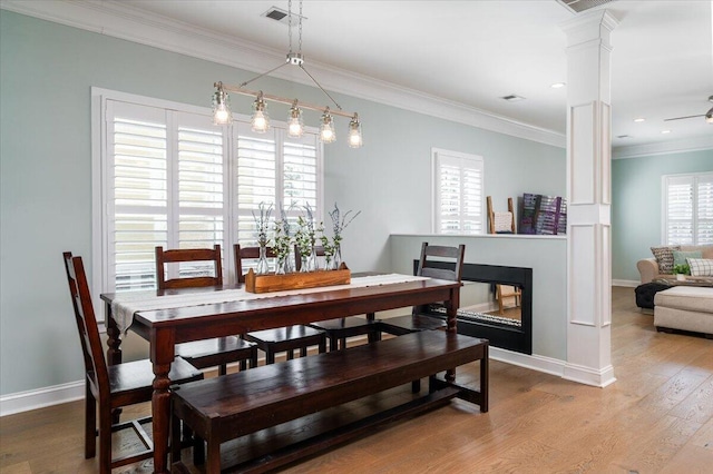 dining room with baseboards, ornamental molding, wood finished floors, ornate columns, and a multi sided fireplace