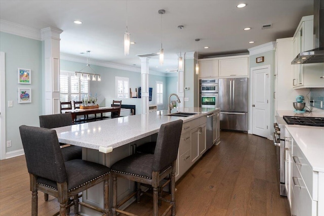 kitchen featuring decorative columns, stainless steel appliances, visible vents, a sink, and wall chimney exhaust hood