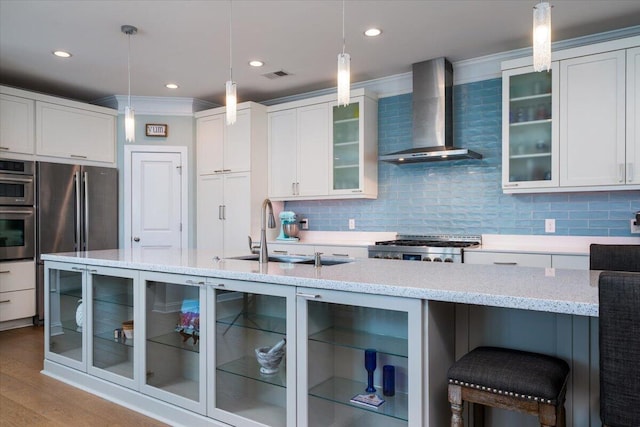 kitchen featuring stainless steel appliances, visible vents, decorative backsplash, a sink, and wall chimney range hood