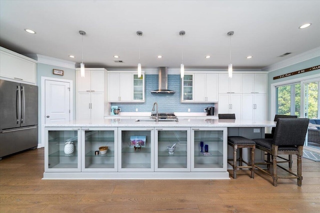 kitchen with a sink, wall chimney range hood, wood finished floors, and freestanding refrigerator