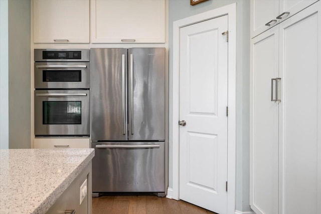 kitchen featuring stainless steel appliances, wood finished floors, white cabinets, and light stone countertops