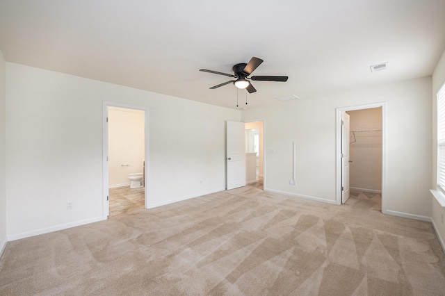 unfurnished bedroom featuring light colored carpet, a walk in closet, baseboards, ensuite bathroom, and a closet