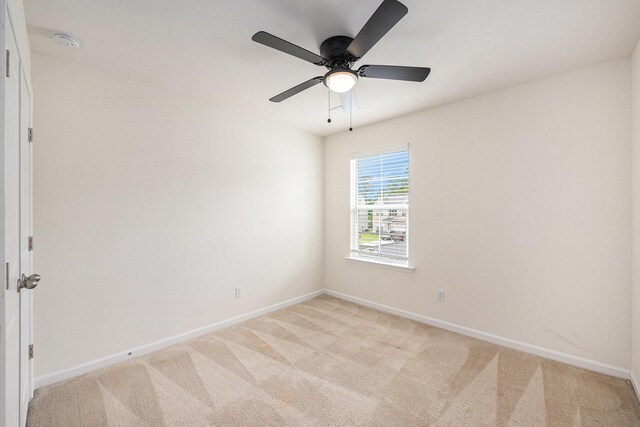 spare room with light colored carpet, baseboards, and a ceiling fan