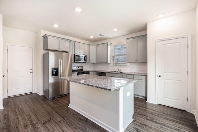 kitchen with stainless steel appliances, gray cabinets, a sink, dark wood-style flooring, and a center island