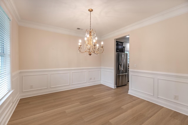 unfurnished dining area with a chandelier, light wood finished floors, crown molding, a wainscoted wall, and a decorative wall