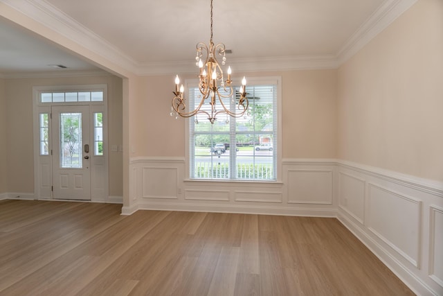 unfurnished dining area featuring light wood-type flooring, healthy amount of natural light, a chandelier, wainscoting, and ornamental molding