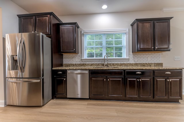 kitchen with appliances with stainless steel finishes, a sink, light wood-style floors, dark stone counters, and dark brown cabinets
