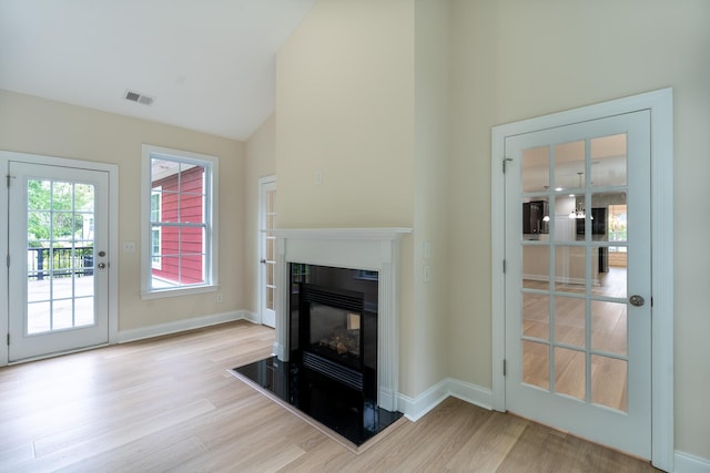unfurnished living room with wood finished floors, a glass covered fireplace, baseboards, and high vaulted ceiling