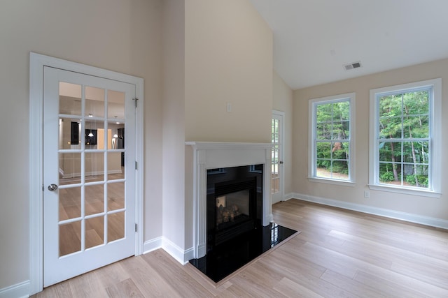 unfurnished living room featuring wood finished floors, a glass covered fireplace, baseboards, and high vaulted ceiling