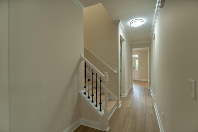 hall with light wood finished floors, crown molding, baseboards, and stairway