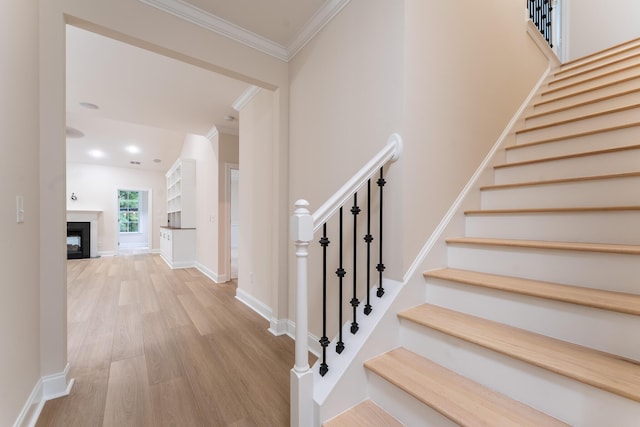stairway featuring ornamental molding, wood finished floors, baseboards, and a fireplace