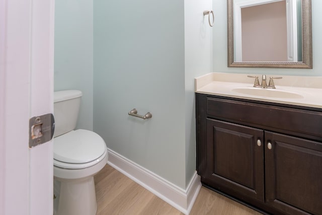 half bathroom featuring baseboards, toilet, vanity, and wood finished floors