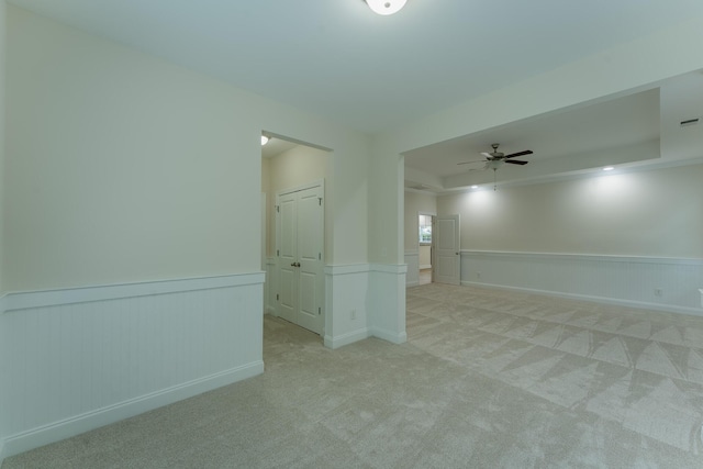 carpeted empty room featuring a wainscoted wall and a ceiling fan