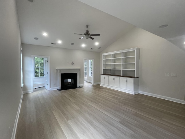 unfurnished living room with a ceiling fan, wood finished floors, a fireplace, vaulted ceiling, and baseboards