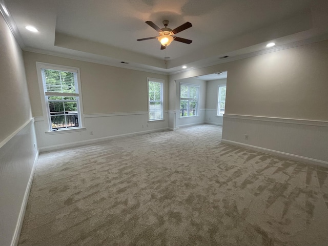 carpeted empty room with a raised ceiling, a ceiling fan, wainscoting, plenty of natural light, and ornamental molding
